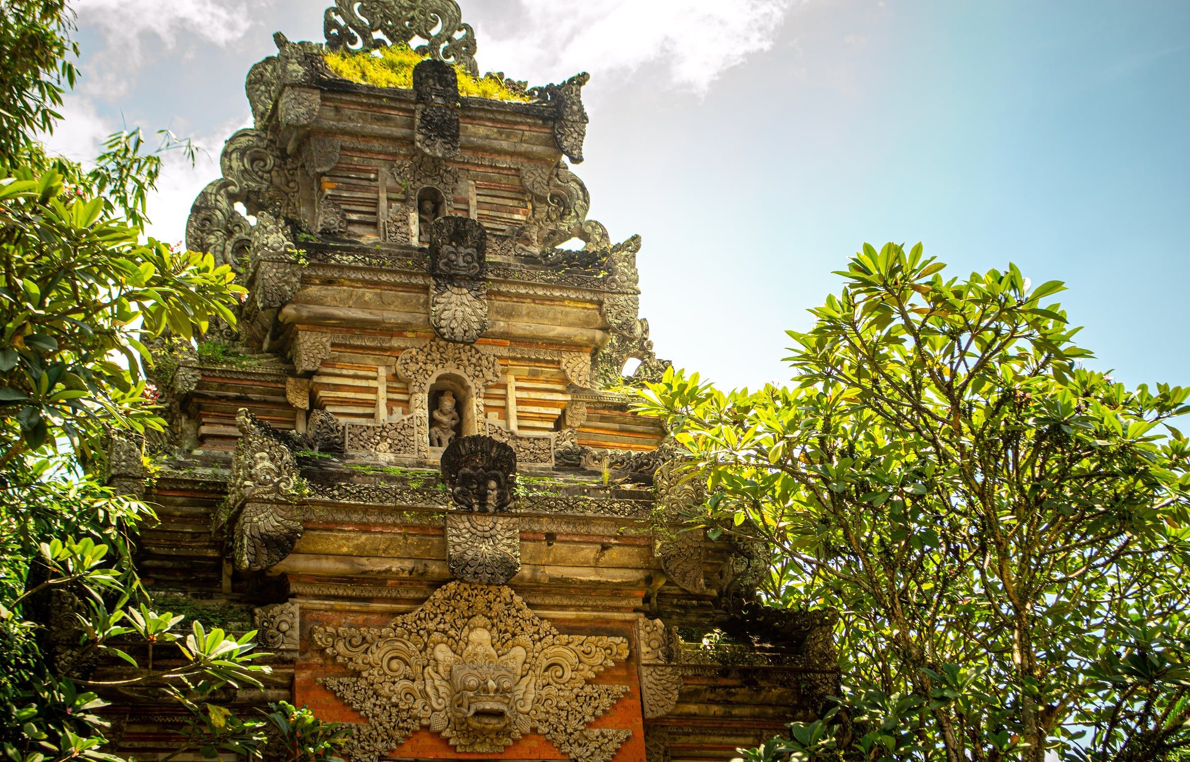 A carved stone gate at Ubud Palace, framed by frangipani trees