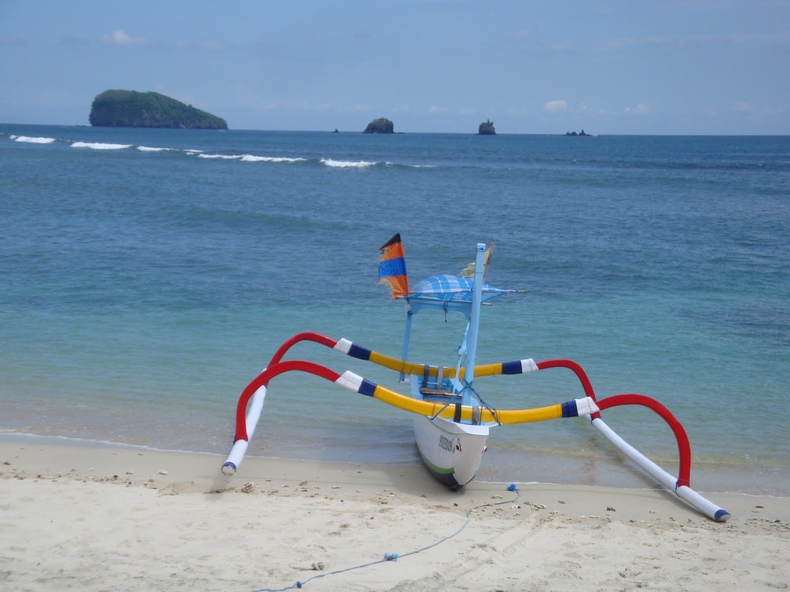 A traditional jukung outrigger on the sand at Candidasa, with the Gili Mimpang islets offshore