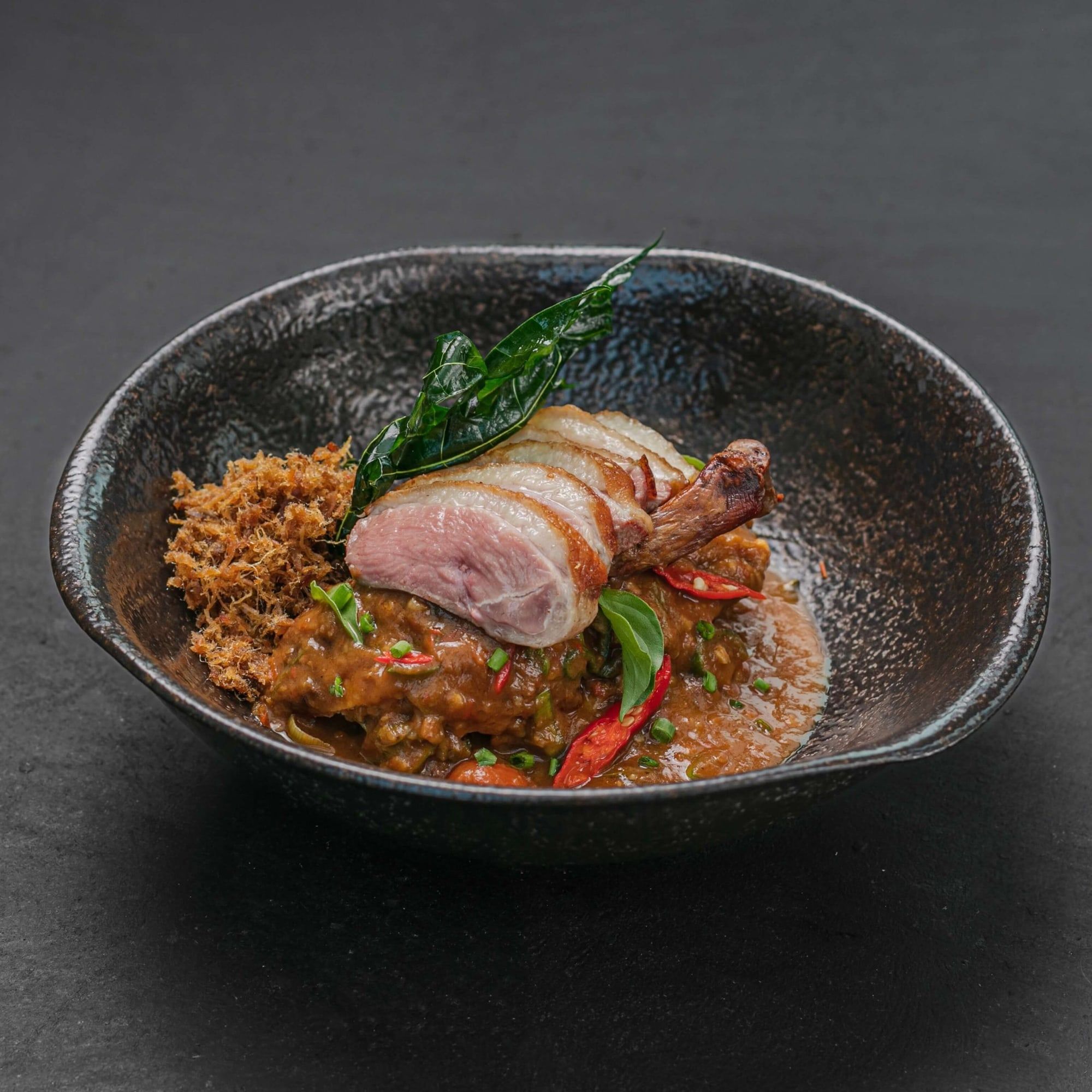 A modern Indonesian dish of sliced meat over spiced rice in a dark stoneware bowl at Merah Putih