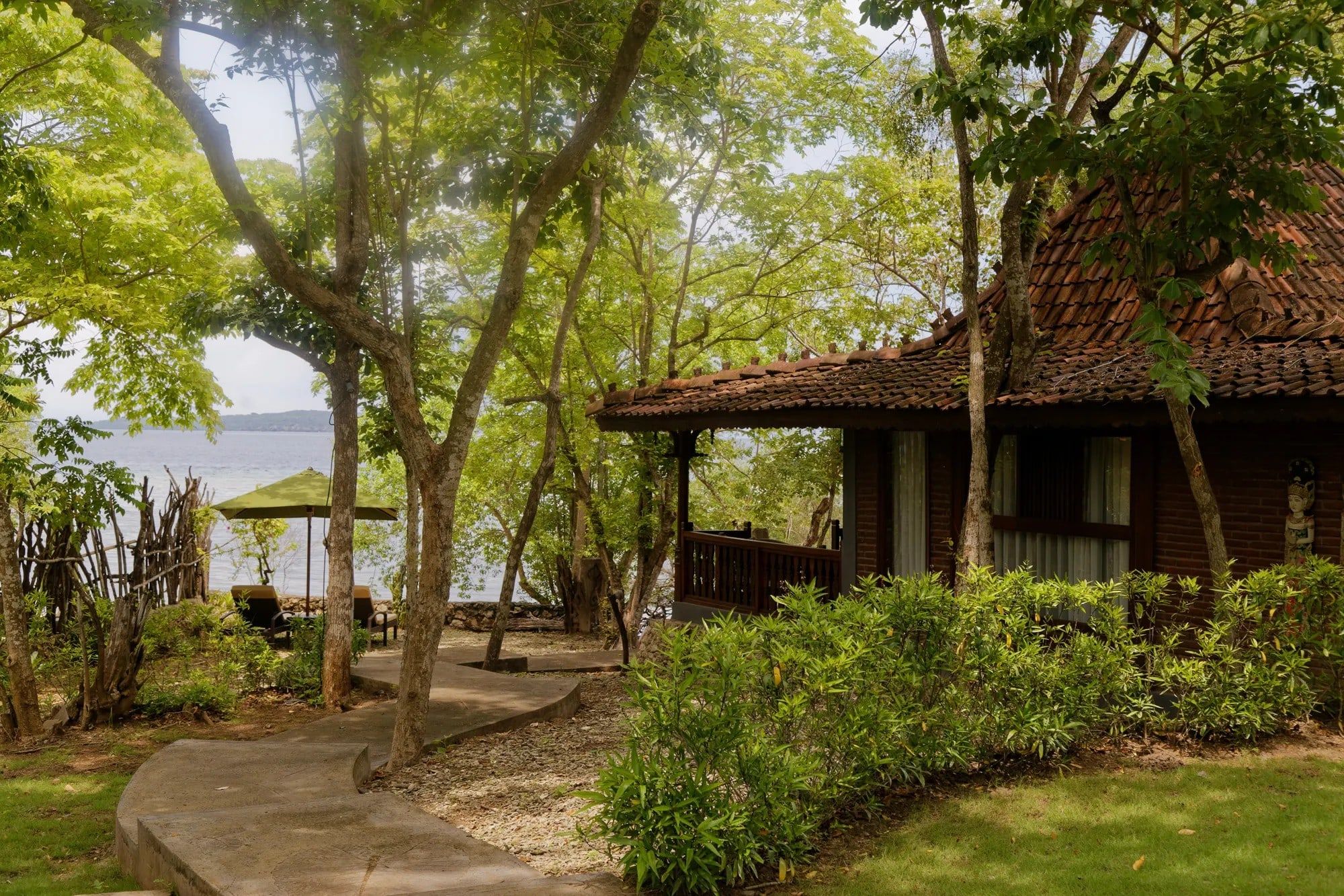 A wooden villa under shade trees by the water at Plataran Menjangan