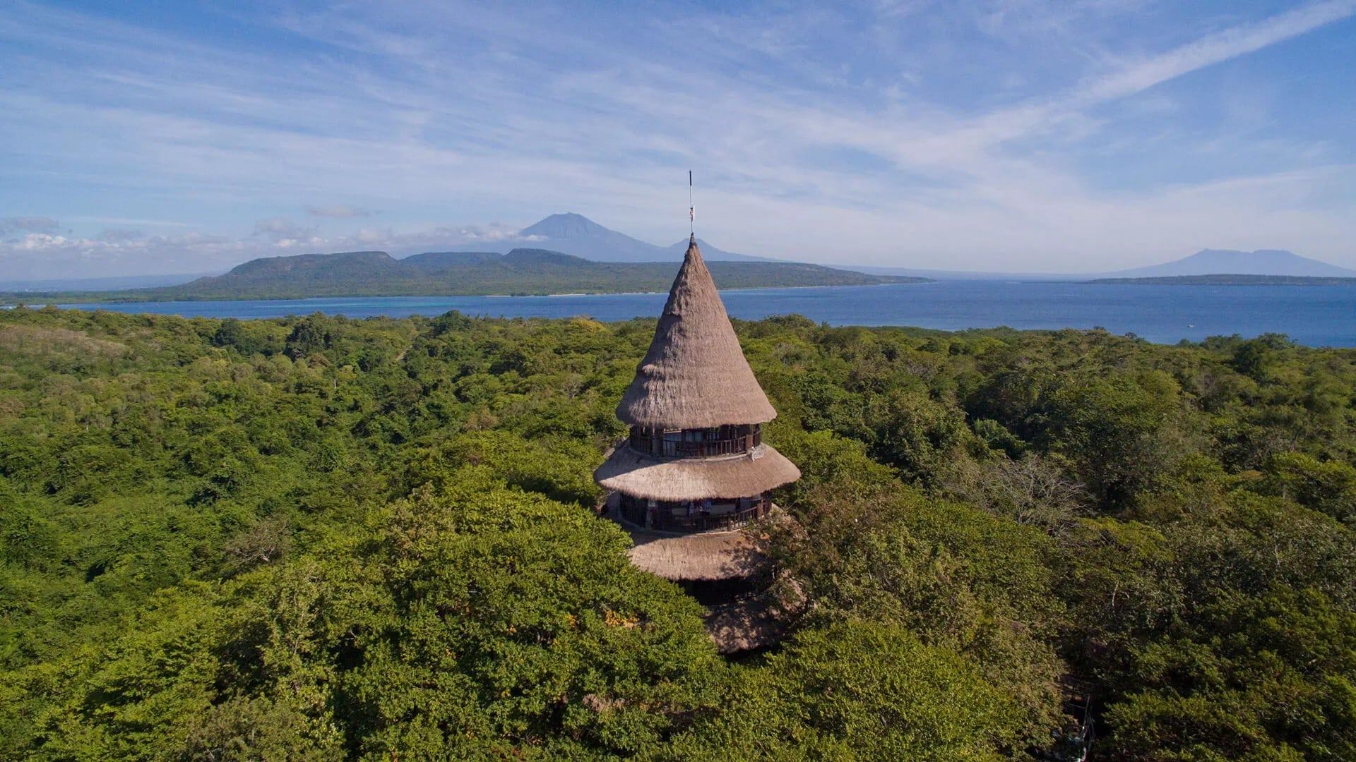 The Menjangan’s thatched lookout tower rising above the forest, with the sea and Java’s volcanoes beyond