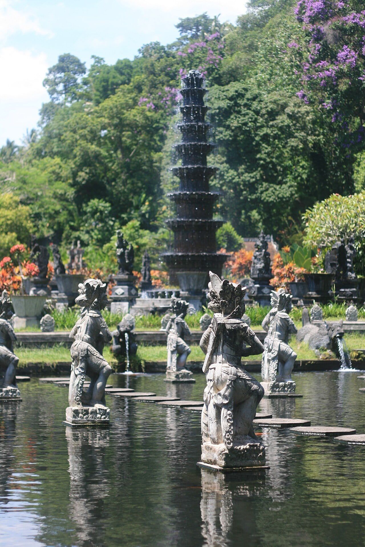 Stepping stones and carved statues in the pools of Tirta Gangga, with the tiered fountain behind
